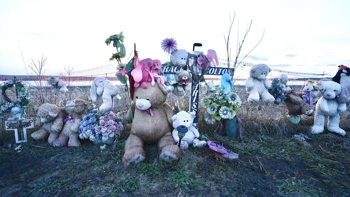 Un monument orné de toutous, de fleurs et d'une croix, rendant hommage aux victimes d'une tragédie.