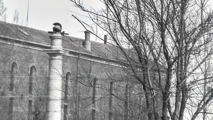Le monument Wolfe, avec sa colonne, son casque et son glaive caractéristiques, se découpe à travers les branches dénudées des arbres, devant la prison des Plaines. 