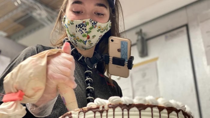 Une jeune femme portant un téléphone à son coup confectionne un gâteau.