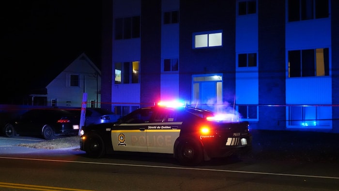 Une autopatrouille de la Sûreté du Québec, gyrophares allumés, est garée devant un immeuble de logements.