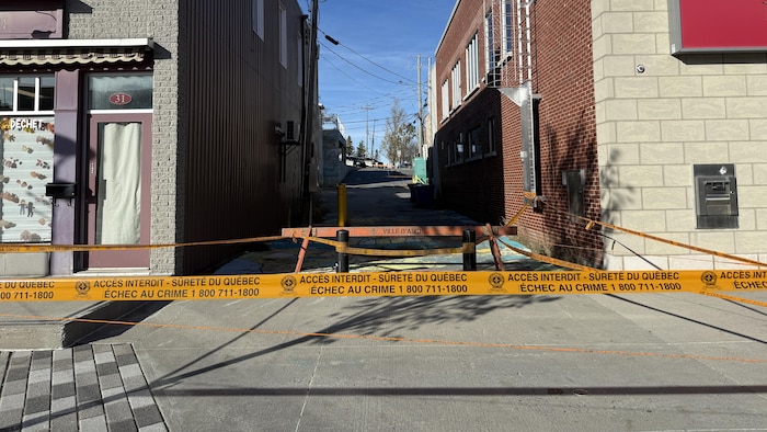 Un ruban de la Sûreté du Québec et une barrière bloquant l'accès à une ruelle.