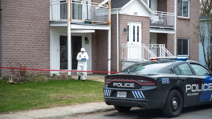 Un technicien en identité judiciaire, en uniforme avec un équipement de protection, sort d'un logement par la porte-patio.