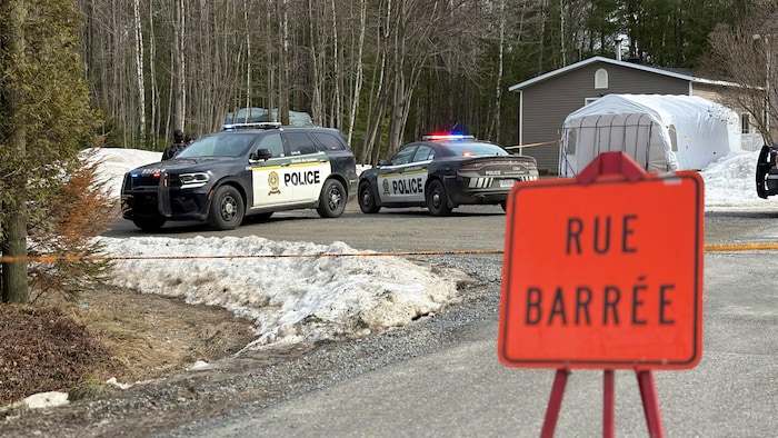 Deux véhicules de police sont immobilisés derrière une pancarte portant la mention de rue barrée, en hiver.