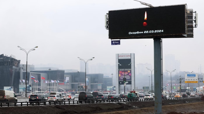 Une route avec des voitures et un panneau avec une bougie allumée au-dessus d'une inscription indiquant, en russe, «nous sommes en deuil». 