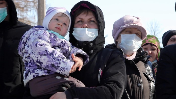 Trois femmes russes portant des masques blancs sur la bouche, se tiennent debout, l'une d'entre elles portant une jeune enfant dans ses bras.