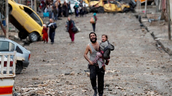 Un hombre transporta a una niña corre escapando de las bombas en Mosul, Irak.