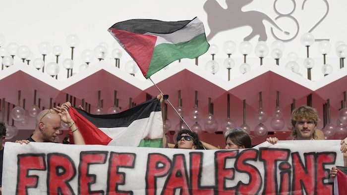 Des manifestants avec des drapeaux et une banderole devant le logo de la Mostra de Venise.