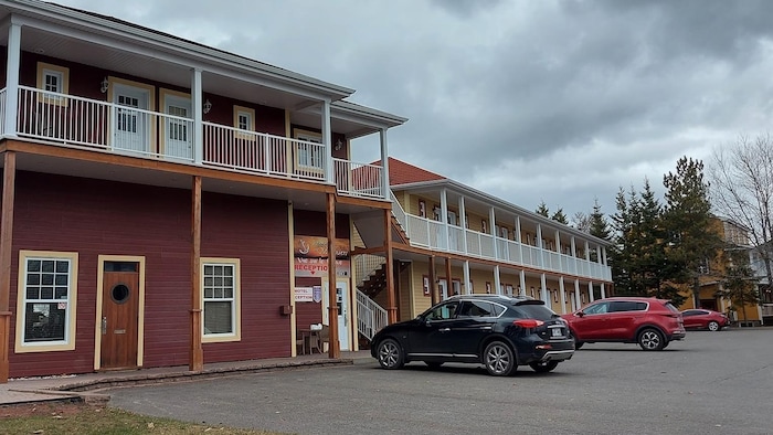 Un bâtiment de type motel avec plusieurs portes et fenêtres alignées sur deux étages et des voitures dans le stationnement. 