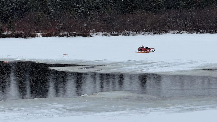 Une motoneige est stationnée sur une rivière partiellement glacée.
