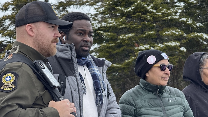 Un policier et trois autres sont photographiés de profil, le regard tourné loin de l'objectif.
