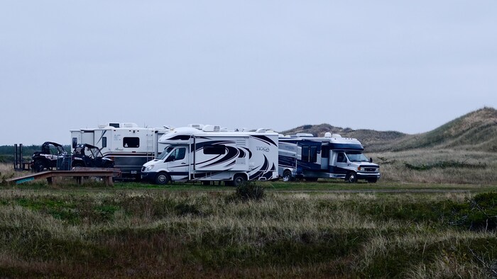 Des motorisés de camping et des quads sont stationnés près des dunes.