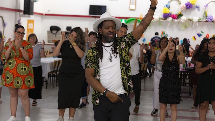Un homme enseigne une chorégraphie à un groupe de danse situé derrière lui.