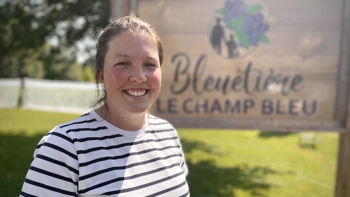 Elle sourit devant un panneau indiquant «bleutière Le champ bleu».