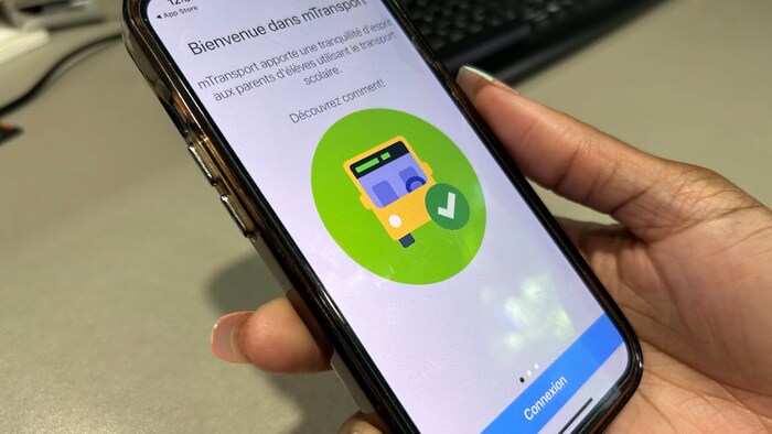 Une main tient un cellulaire avec une application ouverte montrant une illustration d'un autobus scolaire.