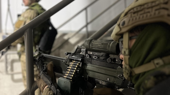 Un militaire pointe sa mitraillette vers la porte d'un bâtiment.