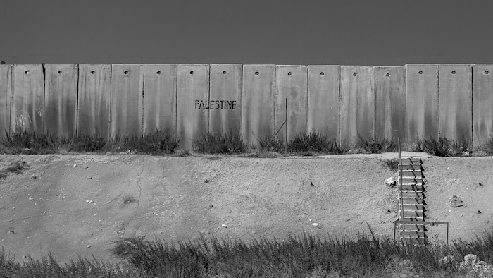 Un long mur de béton porte l'insciption Palestine. 