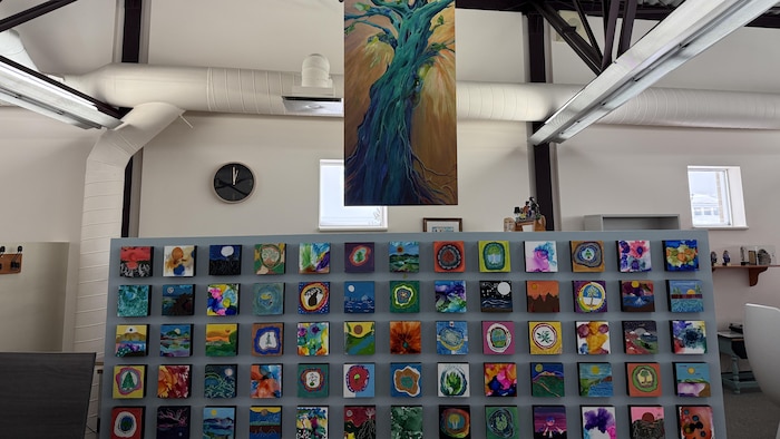 La murale presque complétée. On voit une partie des œuvres individuelles qui forment les racines sous l'arbre peint par l'artiste Guylaine Magny.