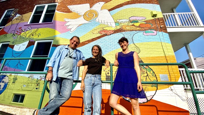 L'artiste peintre Javier Escamilla pose devant la murale de la paix en compagnie de deux artistes collaboratrices, Noémie Veillette et Danahée Cusson.