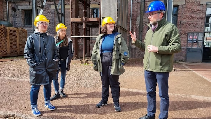 Des personnes avec des casques de construction écoutent un homme qui raconte des choses dans un musée.