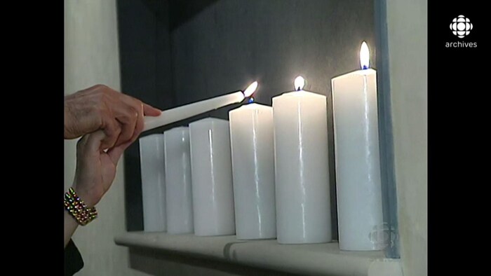 Deux mains tenant une chandelle allument des bougies lors de la cérémonie.