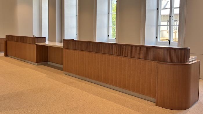 Des comptoirs de réception en bois sont aménagés devant plusieurs fenêtres dans une salle vide.