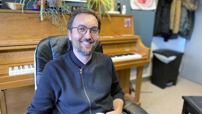 Portrait d'un homme souriant, assis. Derriére lui, un piano en bois. Il s'agit d'Ons Barnat, professeur à la Faculté de musique de l'Université du Québec à Montréal.