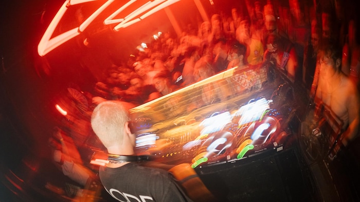 Dans un club, une personne mixe derrière une console et fait face à la foule.