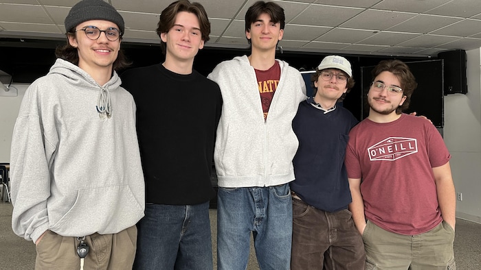 Cinq jeunes hommes posent en rangée.