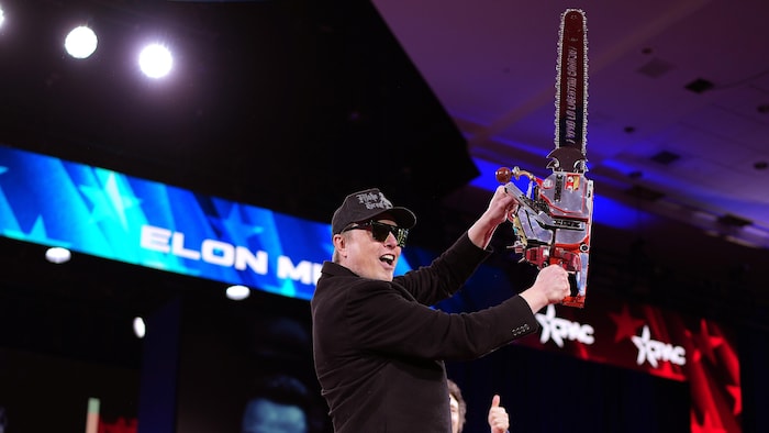 Elon Musk tient une tronçonneuse sur une scène.
