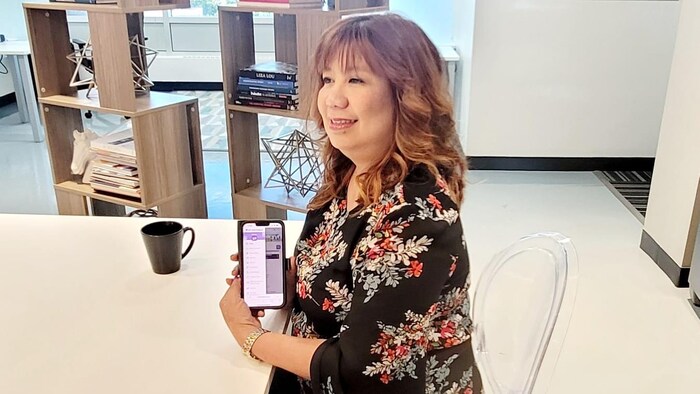 Babae nakaupo malapit sa mesa habang hawak ang isang cellphone.