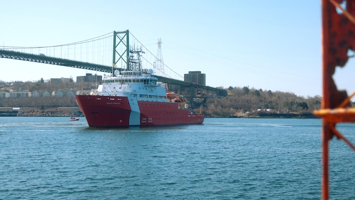 Un grand navire rouge et blanc se tourne vers le port devant un pont à l'arrière-plan.