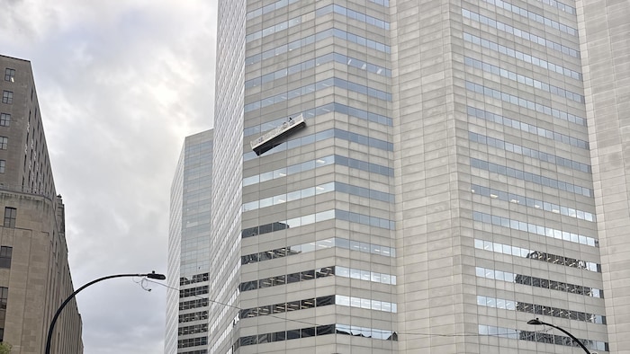 Une nacelle de travaux est suspendue de travers sur la façade d'une tour, au-dessus d'une rue fermée par la police.