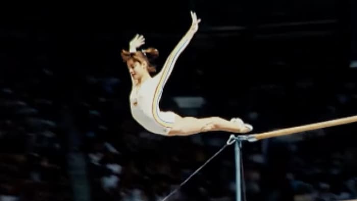 Une gymnaste est archée, lors d'un saut où elle quitte des barres transversales.