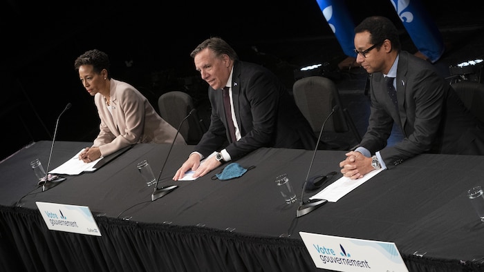Assis à une table, de gauche à droite : Nadine Girault, François Legault et Lionel Carmant.