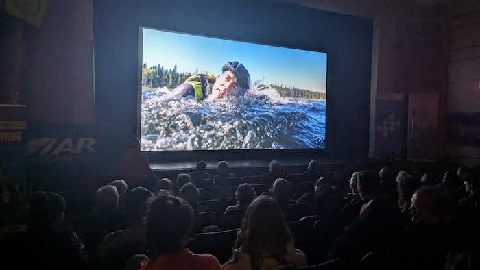 Des gens regardent un écran de cinéma où un homme nage.