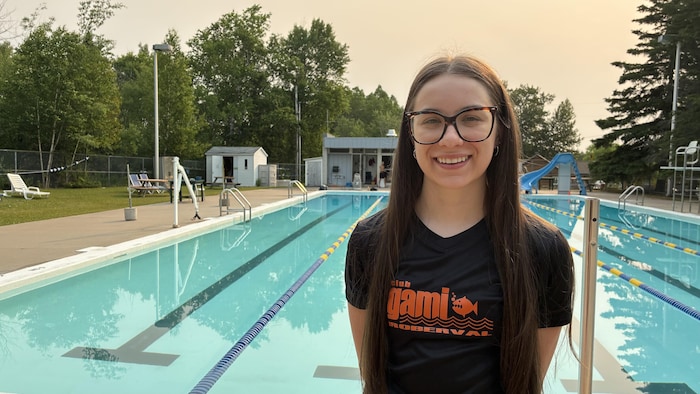 Sandrine regarde l'objectif de la caméra en souriant. Elle se trouve au bord de la piscine.