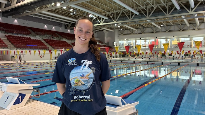 Une jeune femme pose avec un chandail de la Traversée devant une piscine.