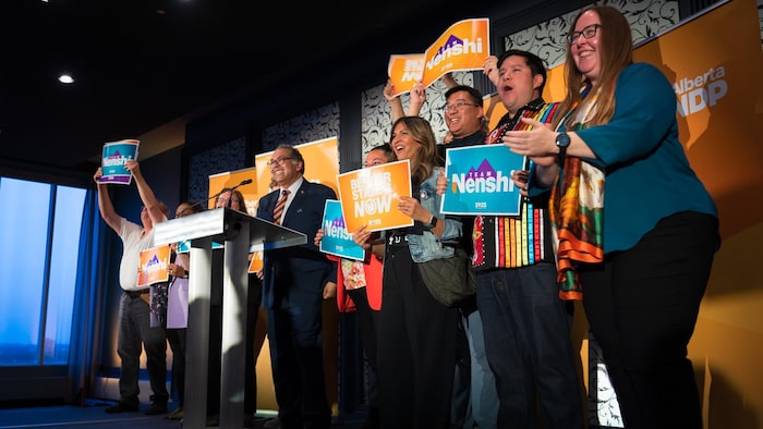 Naheed Nenshi gives a speech to a microphone, in the company of supporters of the NPD.