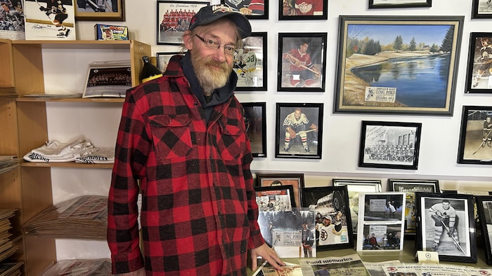 Un homme est debout devant plusieurs photos de joueurs de hockey sur un mur et sur la table. 