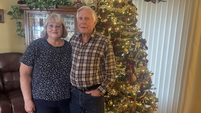 Nancy et Gary Hansen sont debout ensemble devant un sapin de Noël.