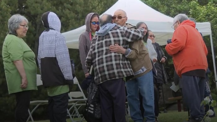 Un groupe de personnes se tient debout, parmi lesquelles deux hommes qui s’étreignent. 