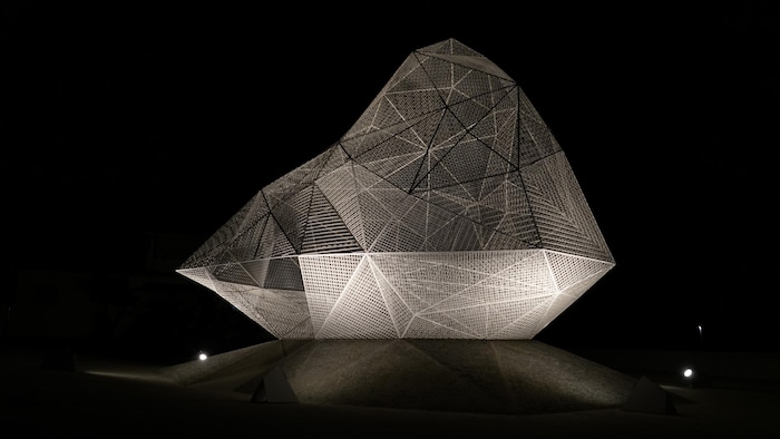 Une œuvre artistique en métal illuminée dans la nuit.