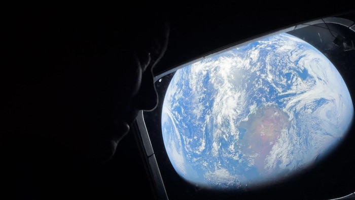 Reid Wiseman regarde la Terre par un hublot.