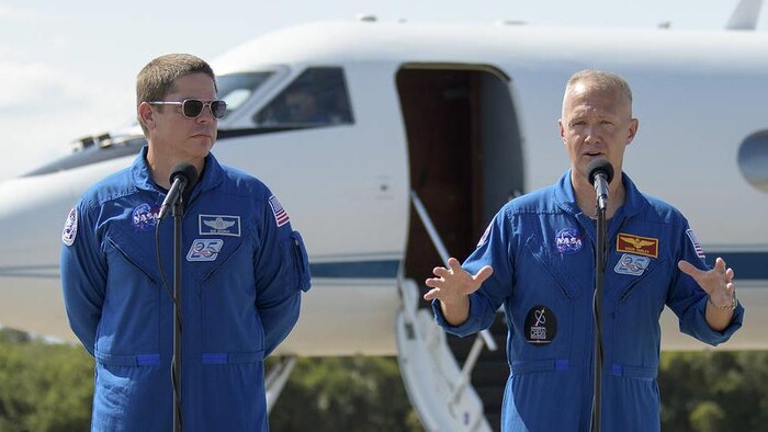 Les astronautes Robert Behnken et Douglas Hurley devant un avion sur une piste de la NASA.