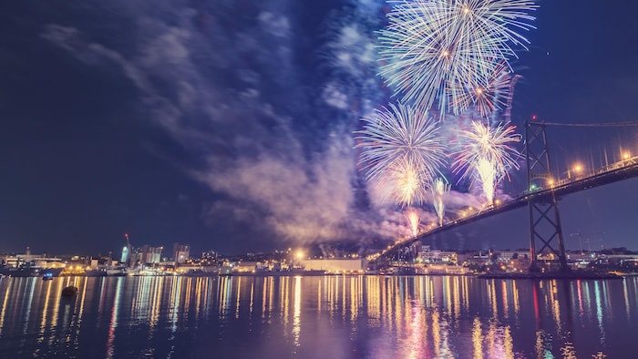 Un ciel la nuit illuminé de feux d'artifice tirés à partir d'un pont et la réflexion des lumières de la ville dans l'eau.