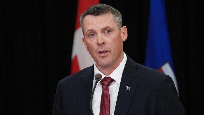 Nate Horner parle à un microphone devant les drapeaux du Canada et de l'Alberta.