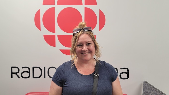 Nathalie Larose-Jolette, lunettes sur la tête, sourit pour la caméra devant le logo de Radio-Canada.