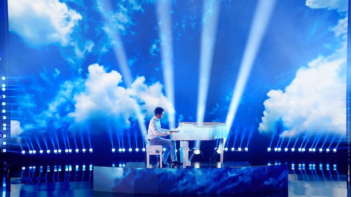 Le pianiste joue sur scène devant un écran géant montrant des nuages.