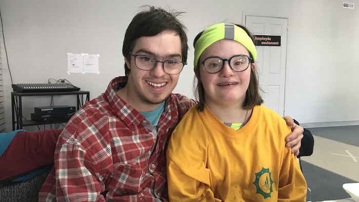Un couple de jeunes adultes trisomiques posent pour la caméra, souriants.