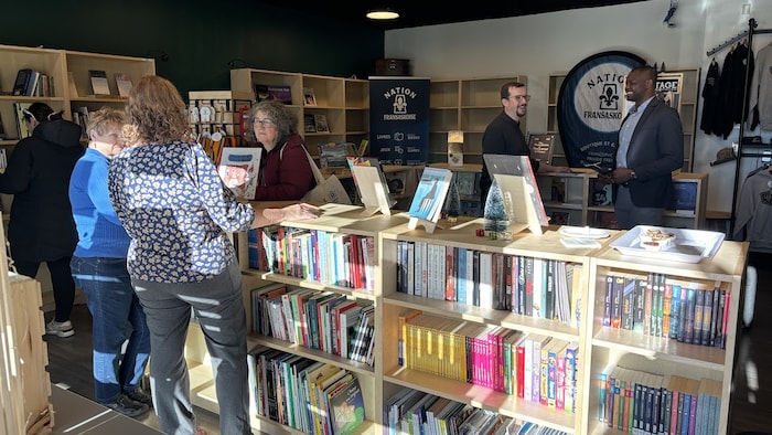 L'intérieur animé de la librairie. Des étagères remplies de livres colorés. Des clients parcourent les livres, certains discutant entre eux.